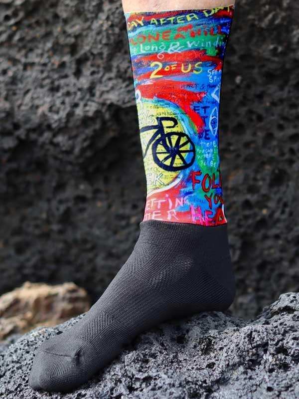 Colorful cycling socks with bike graphics and motivational text, worn on rocky terrain