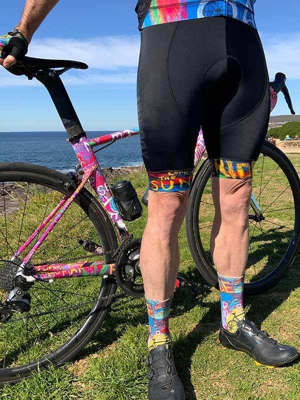 Men's cycling shorts with colorful patterned socks and matching bike, coastal outdoor setting