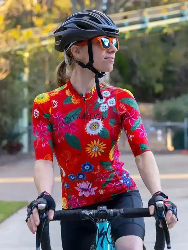 Woman cycling in vibrant floral jersey, helmet, and sunglasses on sunny path