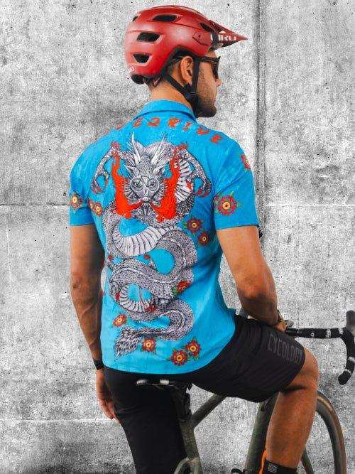Man wearing blue cycling jersey with dragon graphic, red helmet, riding bike against concrete wall