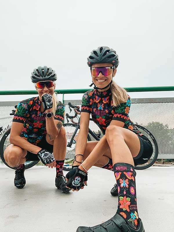 Women in vibrant floral cycling jerseys, helmets, and socks posing with bikes outdoors
