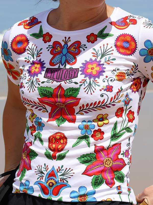 Women's cycling jersey with vibrant floral and butterfly print, featuring colorful flowers and green leaves on white fabric.