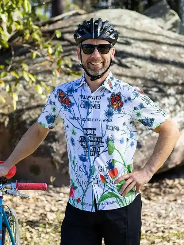Man wearing colorful cycling shirt with butterfly print, helmet, and sunglasses, standing beside bike outdoors