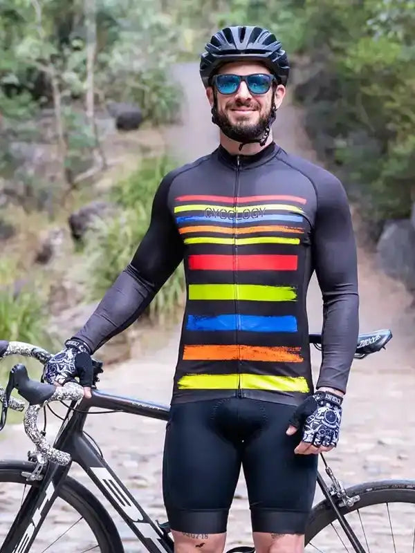 Man in colorful striped cycling jersey and black shorts, standing with road bike on forest trail