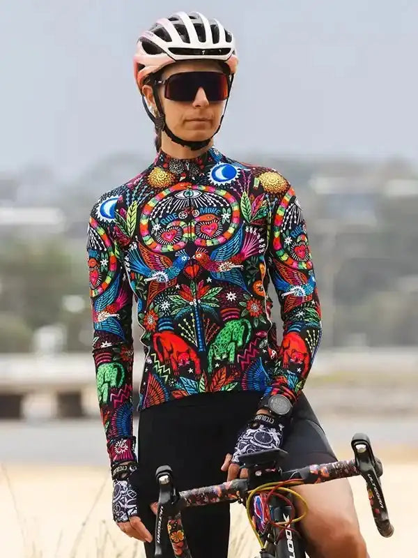 Woman in vibrant, patterned long-sleeve cycling jersey and helmet, holding bike outdoors
