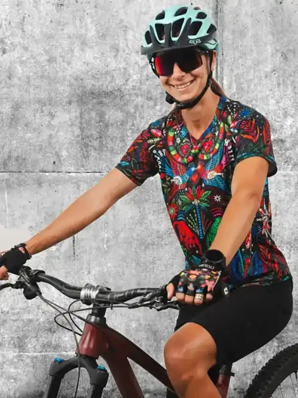 Woman cycling in colorful patterned jersey, helmet, and gloves on mountain bike against concrete wall