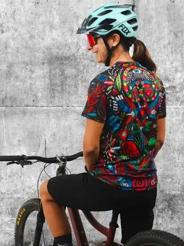 Woman wearing colorful cycling jersey and FOX helmet on bike, urban concrete background