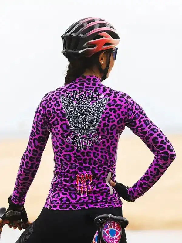 Woman in purple leopard print cycling jersey with 'Bad Ass Kitty' graphic, wearing helmet and gloves