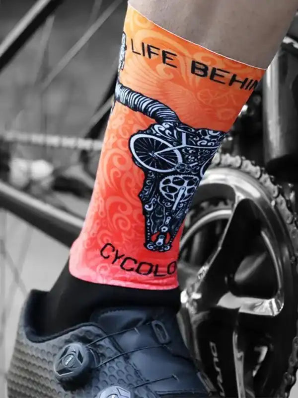 Orange cycling sock with skull and bike design, worn with road bike shoe