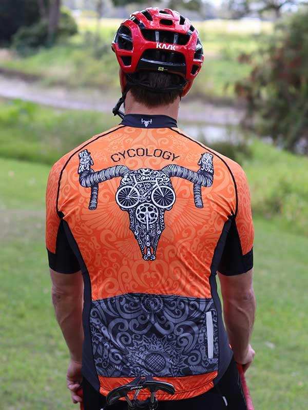 Men's orange cycling jersey with skull and bike graphic, worn with red helmet outdoors