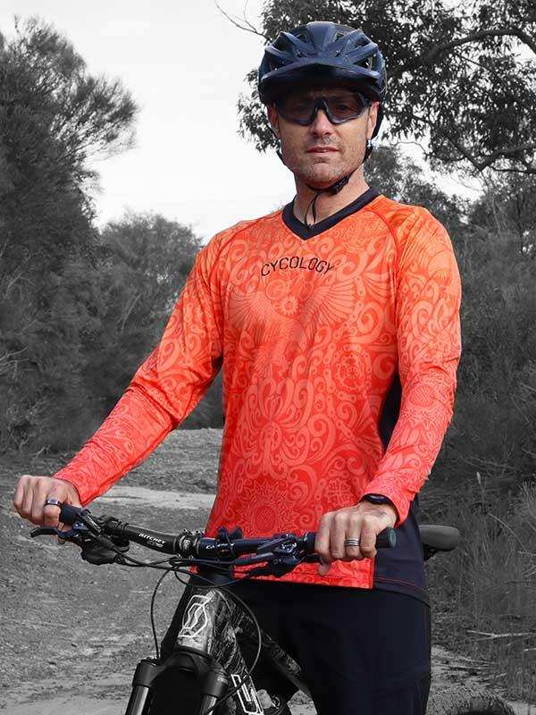 Man wearing orange patterned long sleeve cycling jersey and helmet on mountain bike trail
