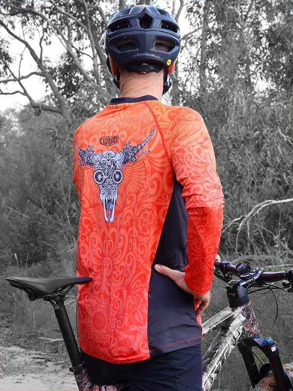 Men's orange cycling jersey with skull graphic, worn with helmet on trail ride