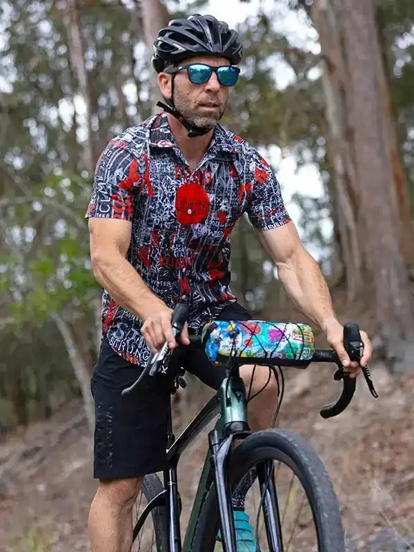 Man cycling in patterned jersey and black shorts, wearing helmet and sunglasses on forest trail
