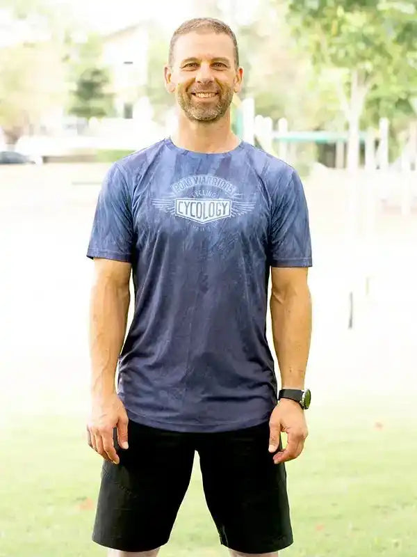 Man wearing blue cycling t-shirt with 'Cycology' logo, black shorts, outdoors on grass
