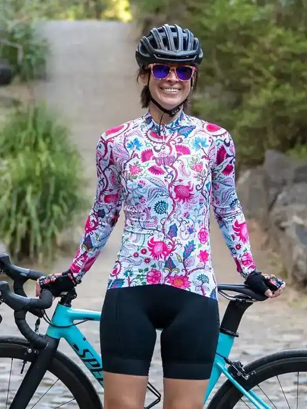Woman in colorful floral cycling jersey and black shorts, standing with bike outdoors