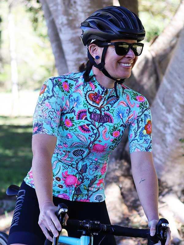 Woman cycling in vibrant floral jersey and black shorts, wearing helmet and sunglasses outdoors