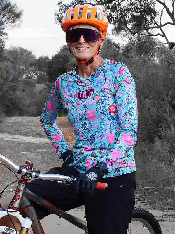 Woman in colorful floral cycling jersey and orange helmet on mountain bike trail