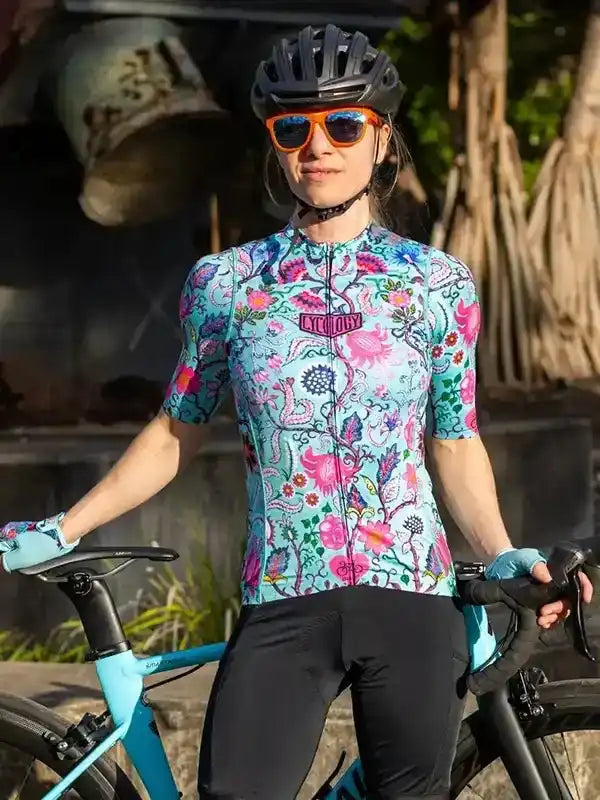 Woman in floral cycling jersey and helmet, holding bike outdoors