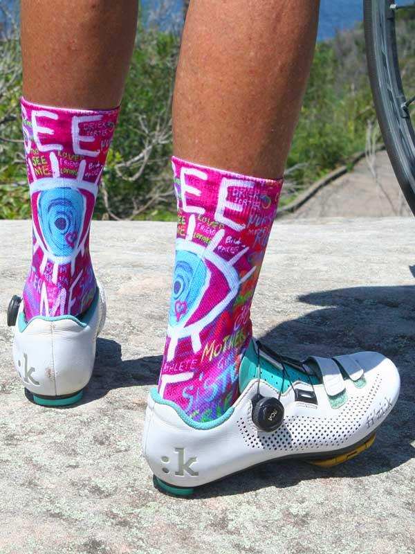 Vibrant pink cycling socks with bold graphic design, worn with white road bike shoes on outdoor trail