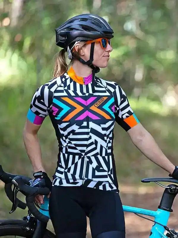 Woman in colorful geometric cycling jersey and helmet, standing with road bike in forest