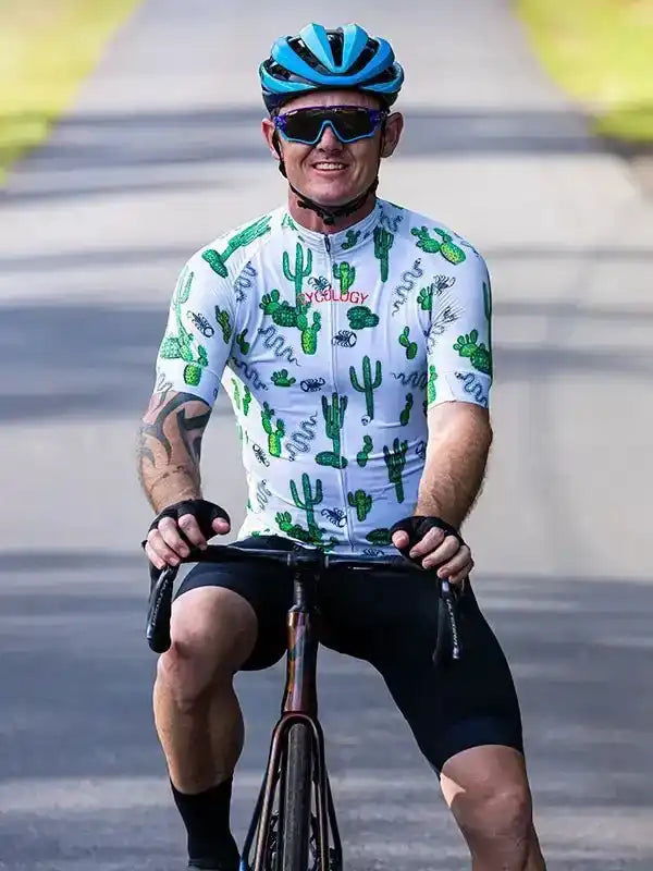 Man cycling in cactus-print jersey, helmet, and sunglasses on paved road