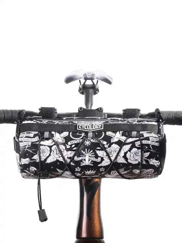 Black and white tattoo-style cycling handlebar bag with rose and wing designs, mounted on bike