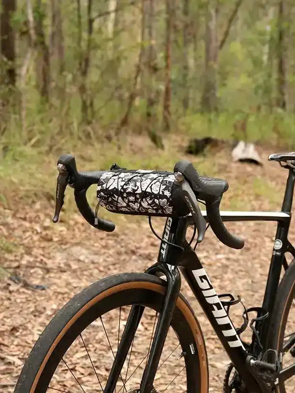 Black Giant road bike with floral handlebar bag in forest setting, ideal for cycling adventures