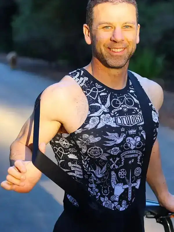 Man wearing black cycling tank top with white tattoo-style graphics, outdoors on bike path