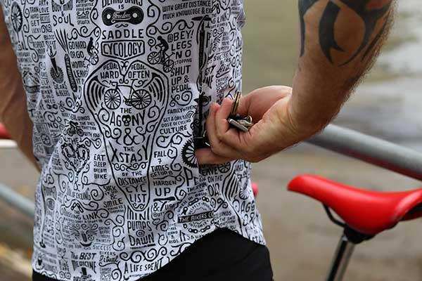 Men's cycling jersey with bold graphic print, featuring bike-themed typography and designs, worn by cyclist near red saddle.